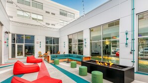 A modern outdoor seating area with red and green chairs, a black fire pit, and a large window overlooking a parking area. - Aloft by Marriott Anchorage (Anchorage)