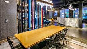 A modern interior with a long wooden table and chairs, a colorful vertical partition, and a contemporary light fixture. - Aloft by Marriott Anchorage (Anchorage)