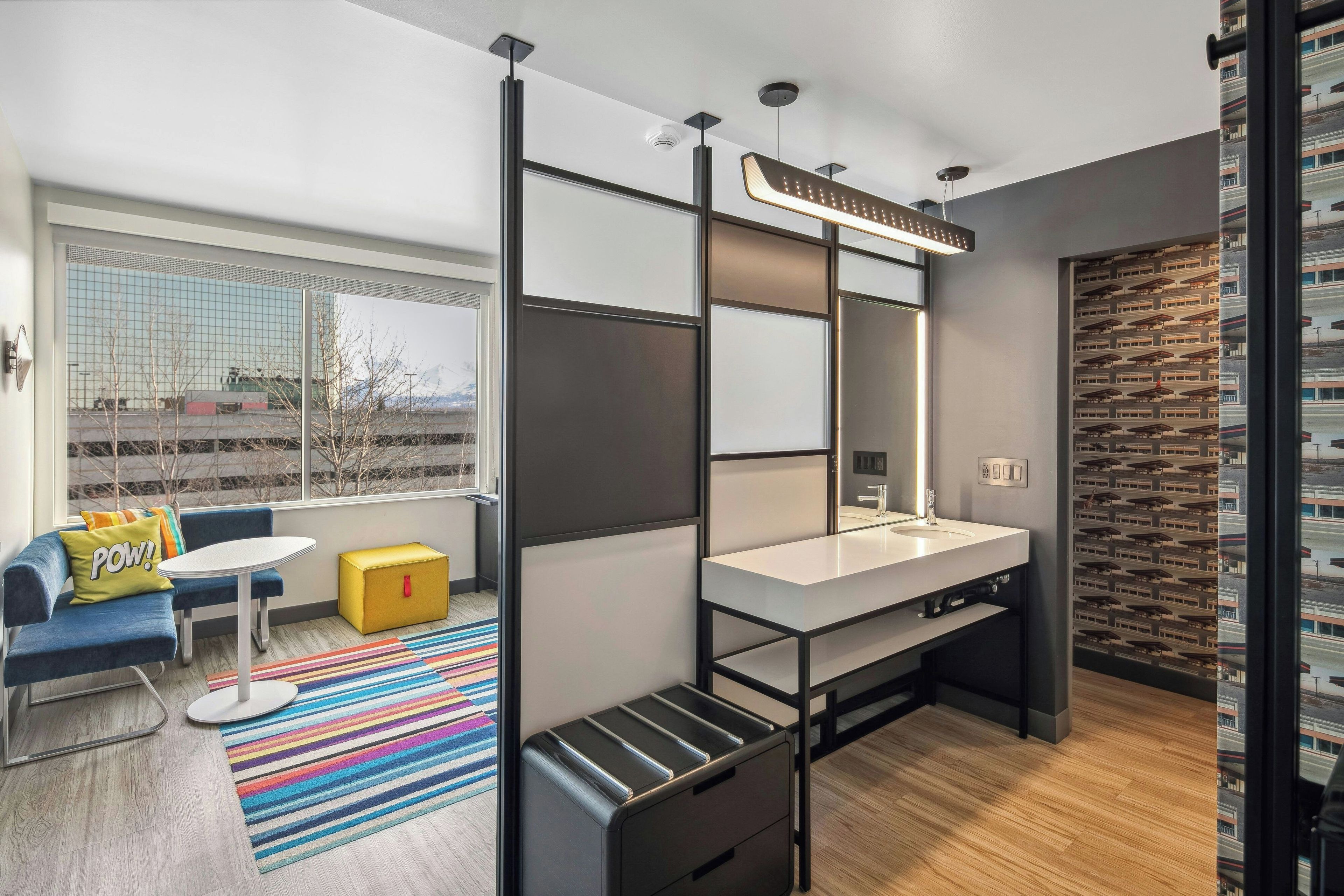 A modern bathroom with a large mirror, a sink, and a shower area. There is a window providing a view of the outside.
