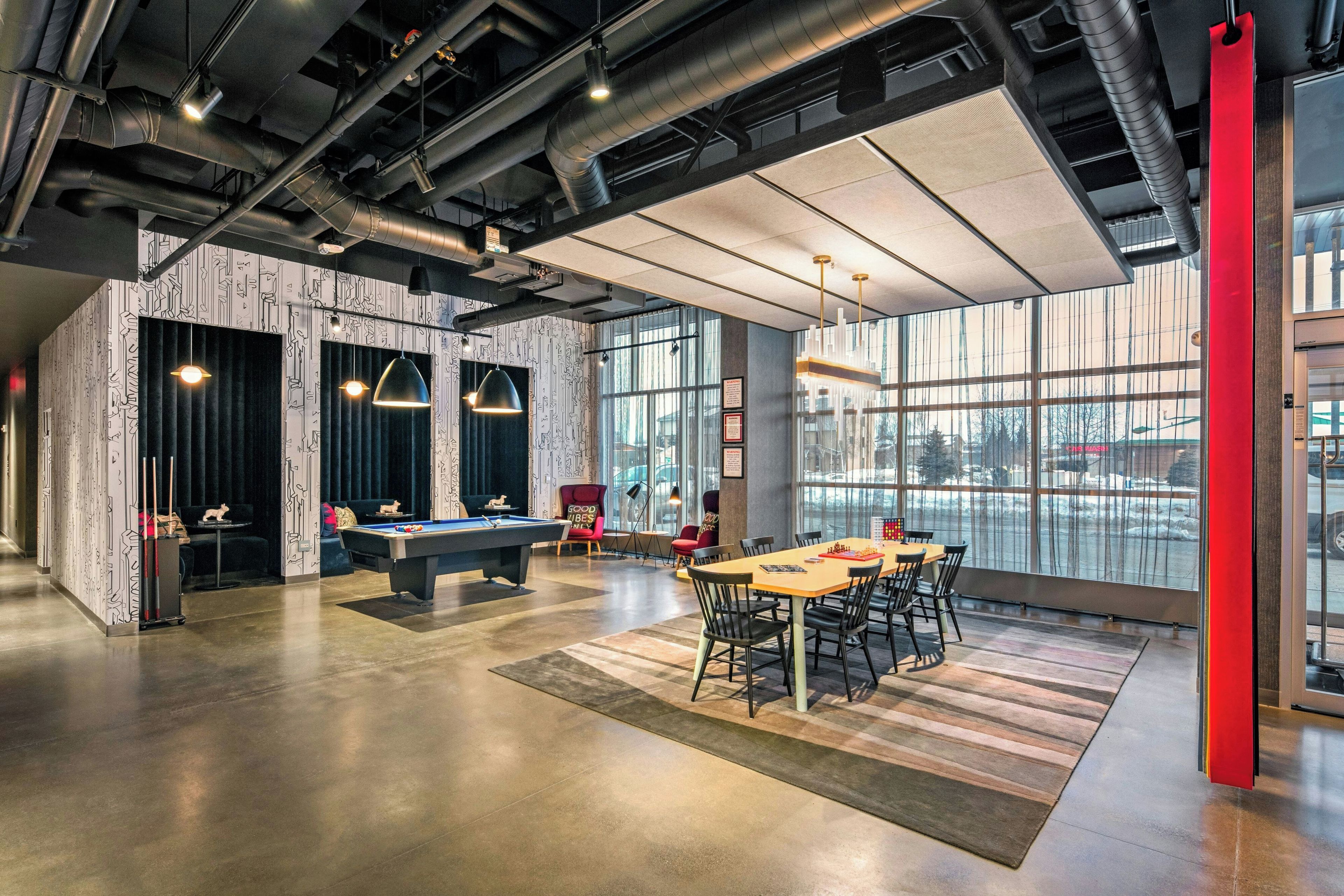 A modern indoor space with a pool table, billiards, a dining area, and large windows offering a view.