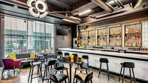A modern bar area with a bar counter, stools, and a seating area with a sofa and chairs. - Aloft by Marriott Anchorage (Anchorage)