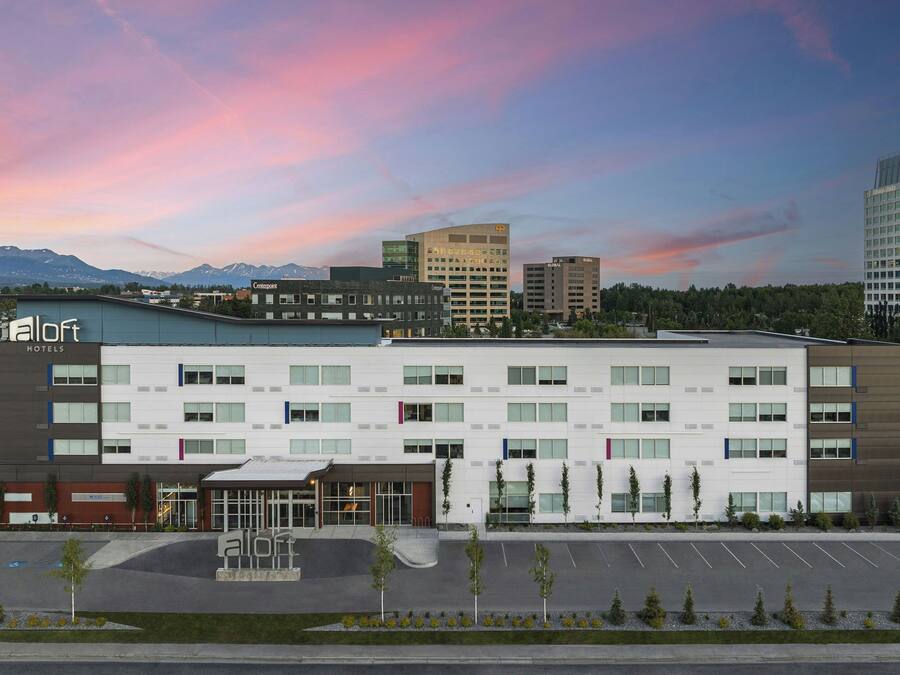 A hotel with a modern design, featuring a flat roof and a parking lot in front.