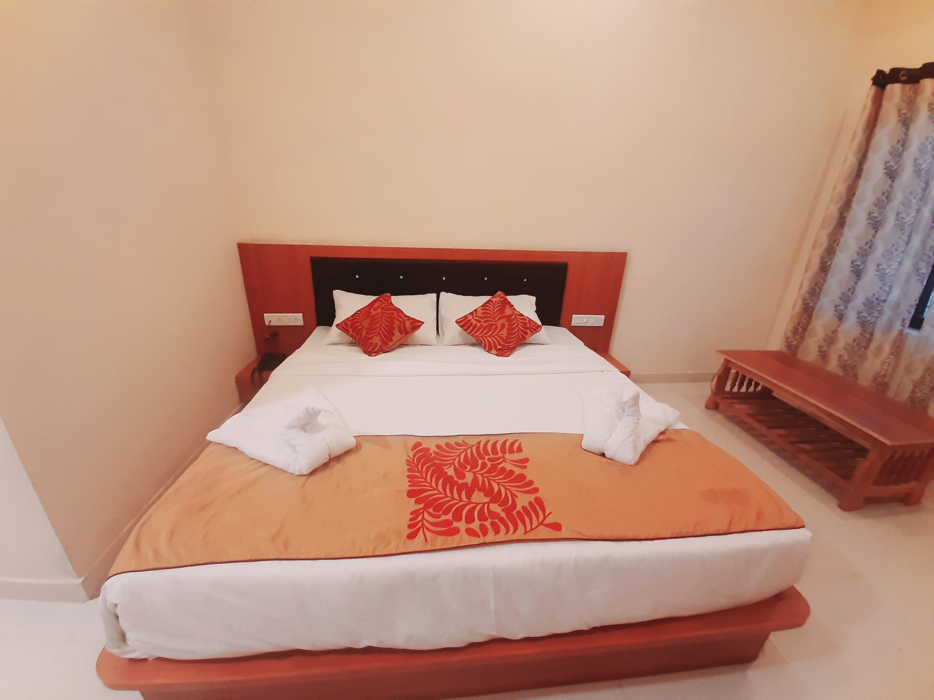 A neatly made bed with a red and white patterned bedspread, two red pillows, and a wooden bench beside the bed.