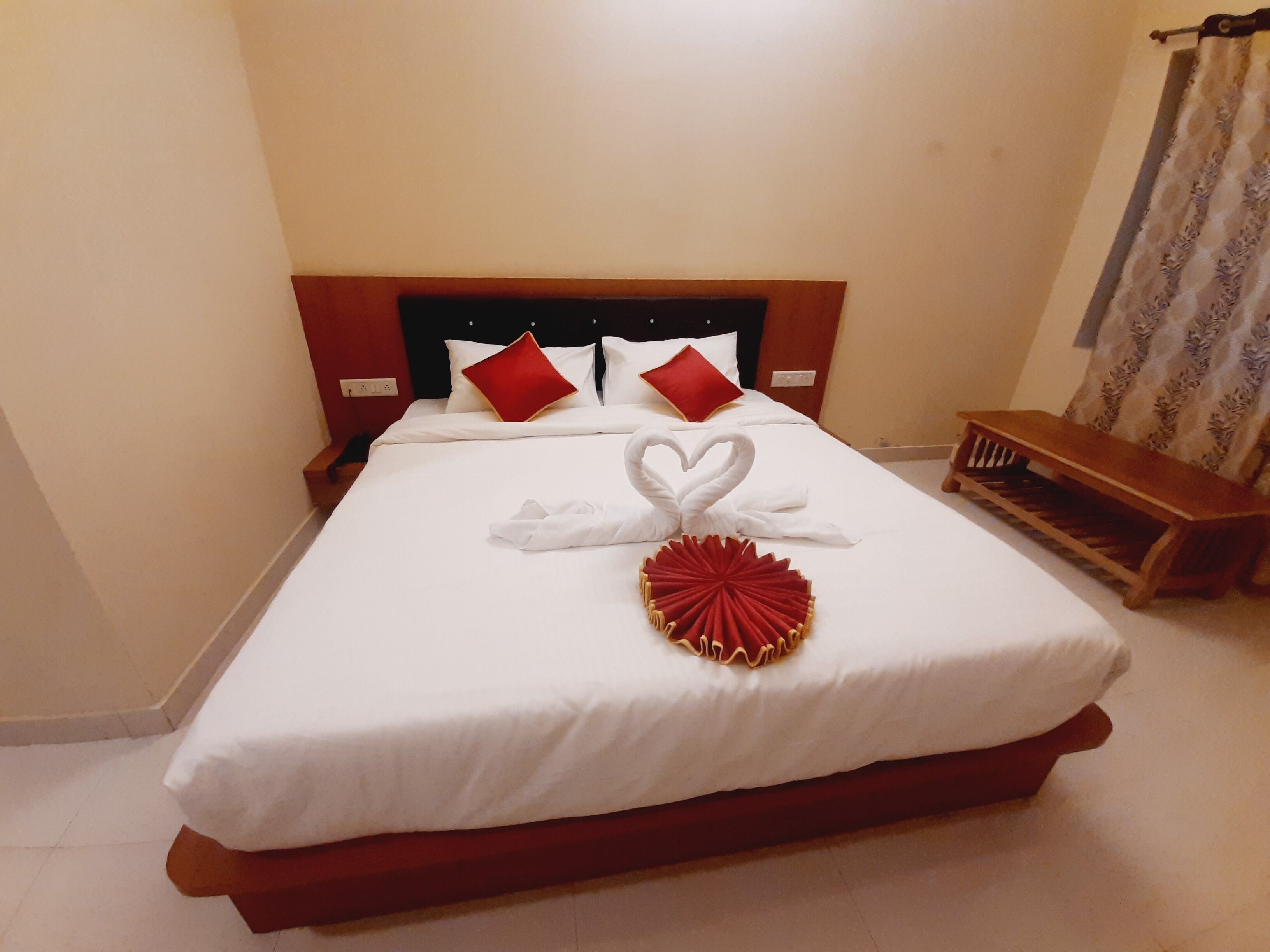 A neatly made bed with white bedding, two red pillows, and a heart-shaped towel arrangement.