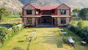 A two-story building with a stone facade and red roof, surrounded by a well-maintained lawn and outdoor seating area. - Pushkar Retreat Resort (Pushkar)