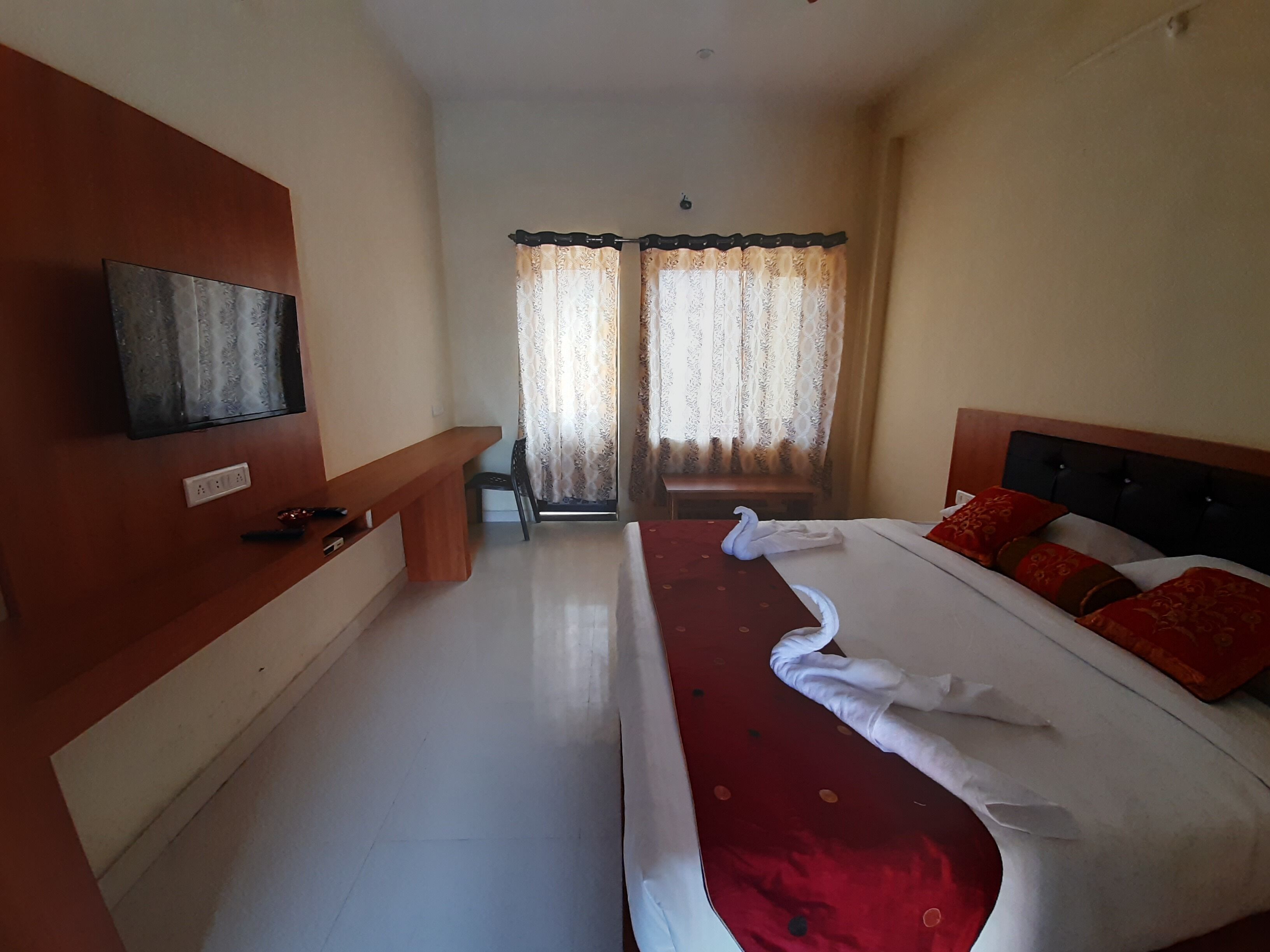 A hotel room with a bed, a TV mounted on the wall, a bench, and a window with curtains.