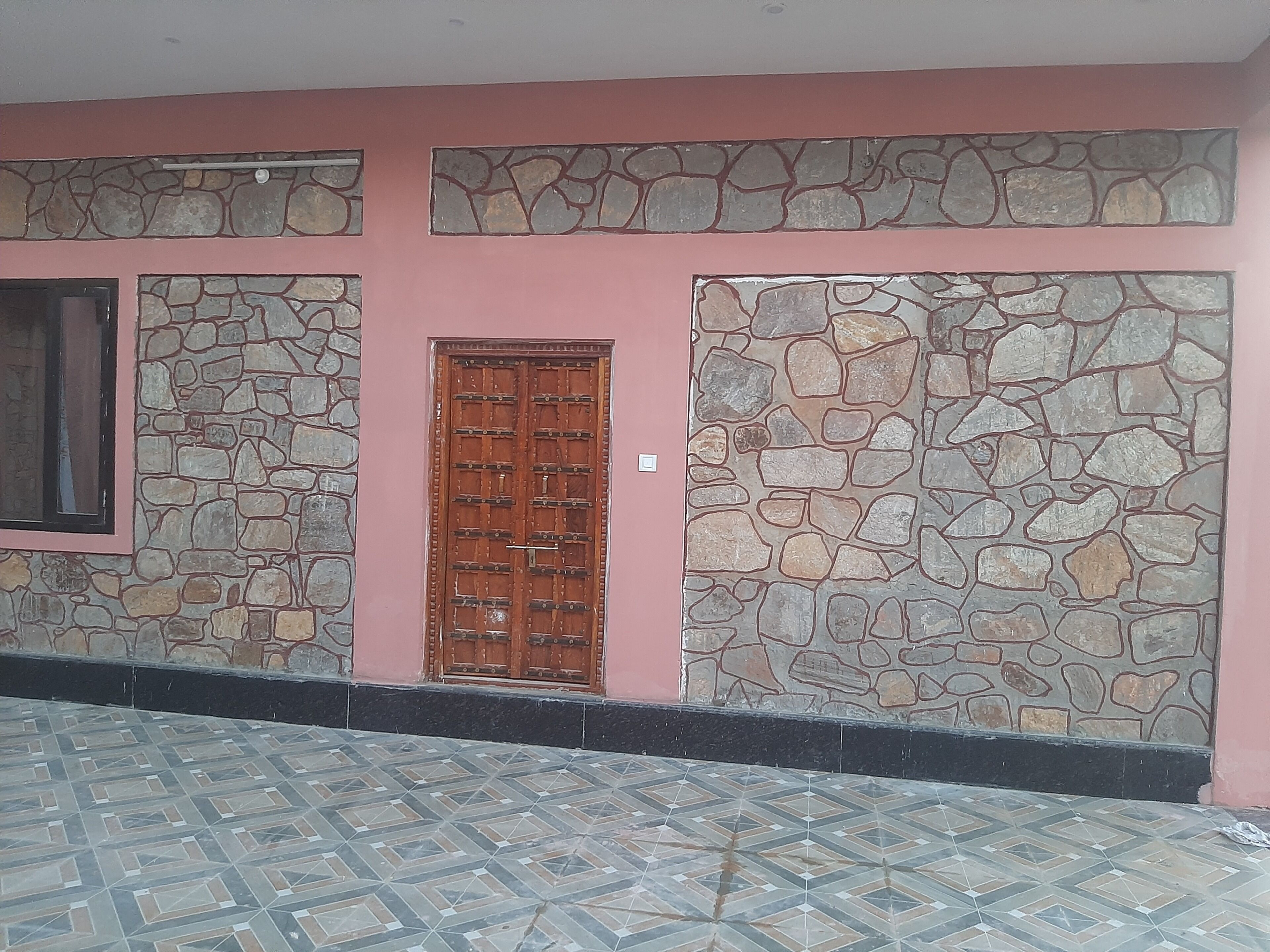 Fachada de edificio con pared de piedra, puerta de madera y suelo de baldosas.
