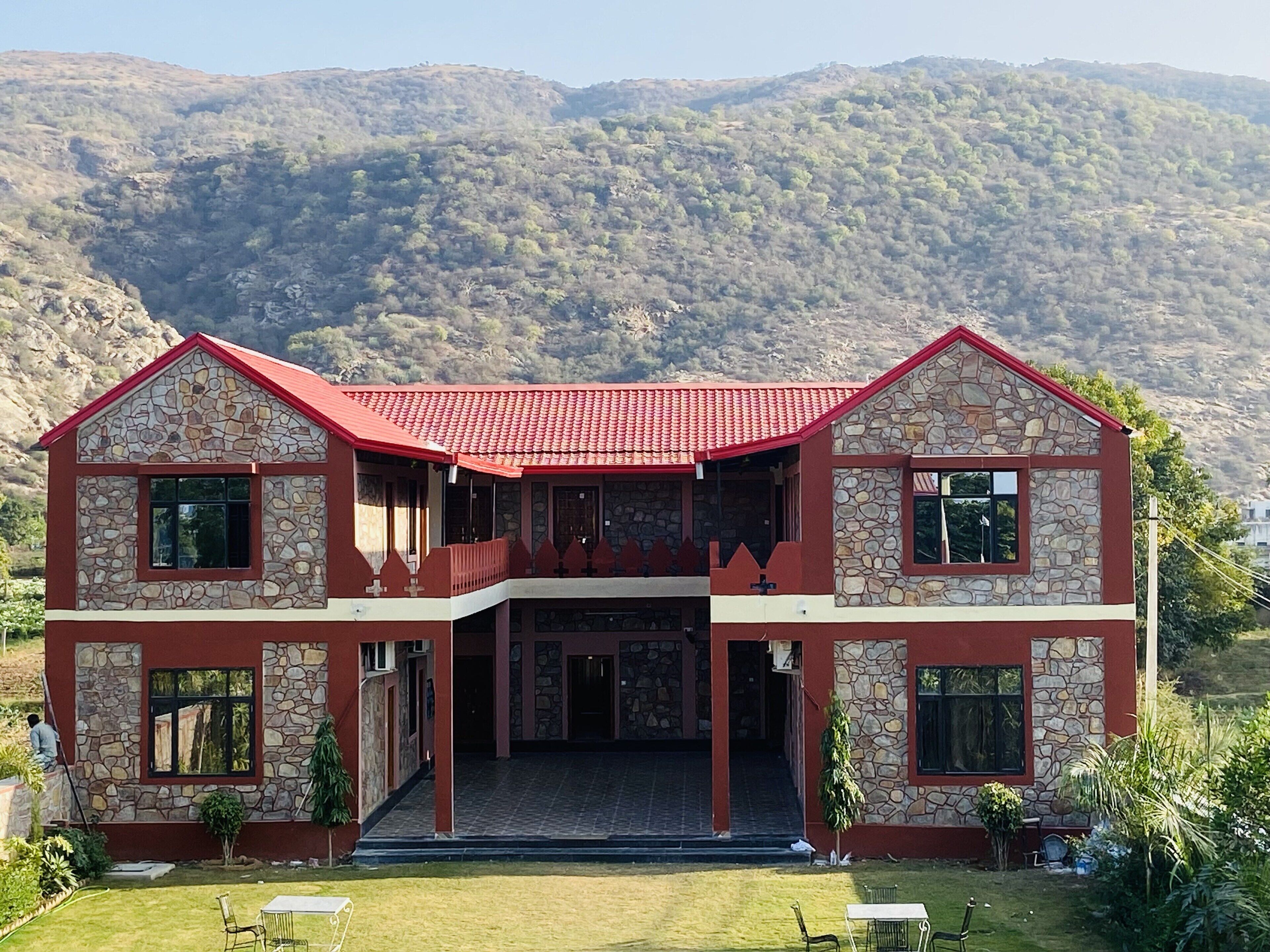 A two-story stone building with a red roof, a balcony, and a front entrance.