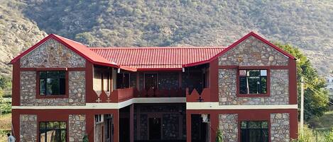 A two-story stone building with a red roof, a balcony, and a front entrance.