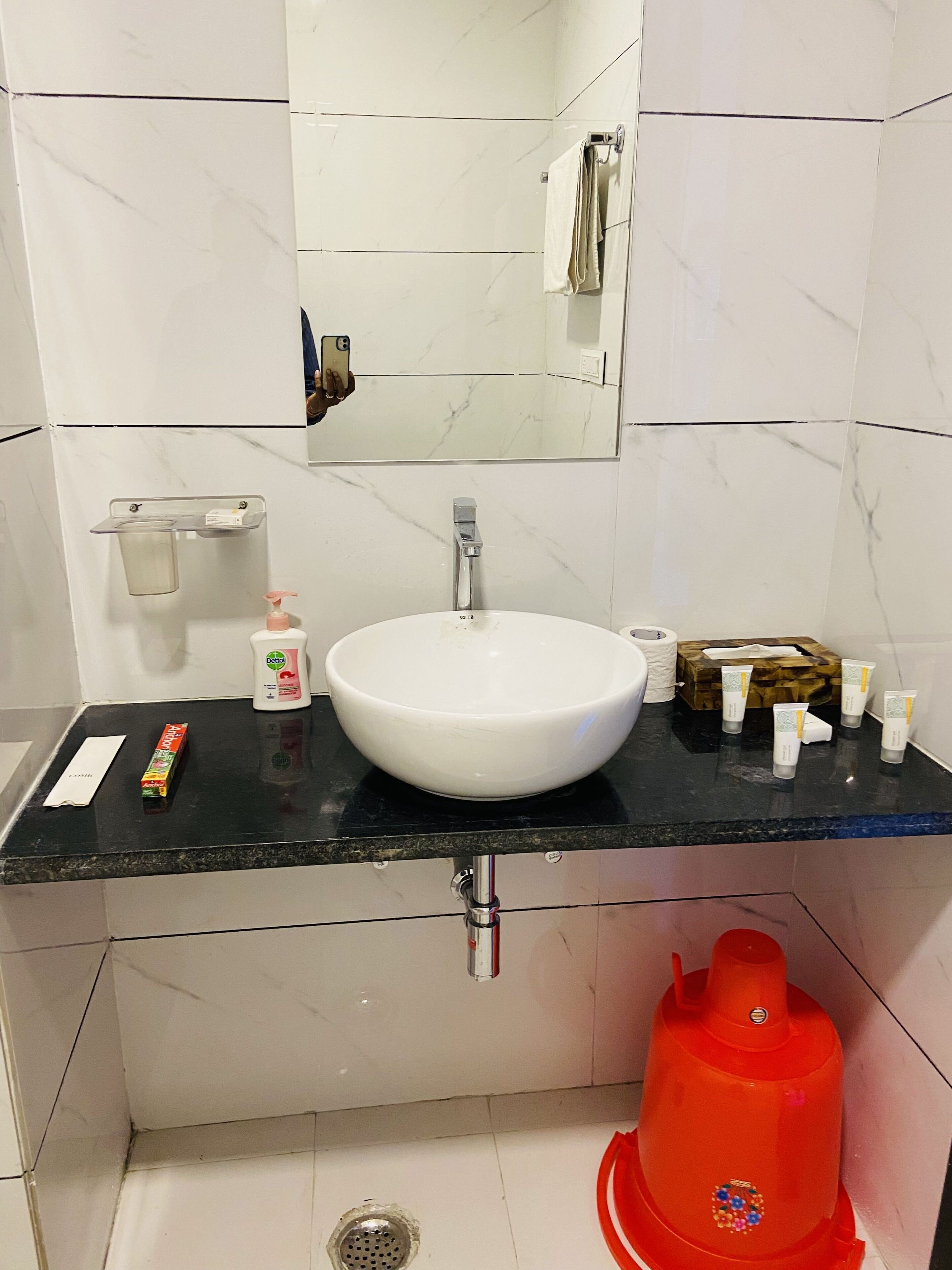 A bathroom with a white sink, a mirror, a black countertop, and a red bidet.