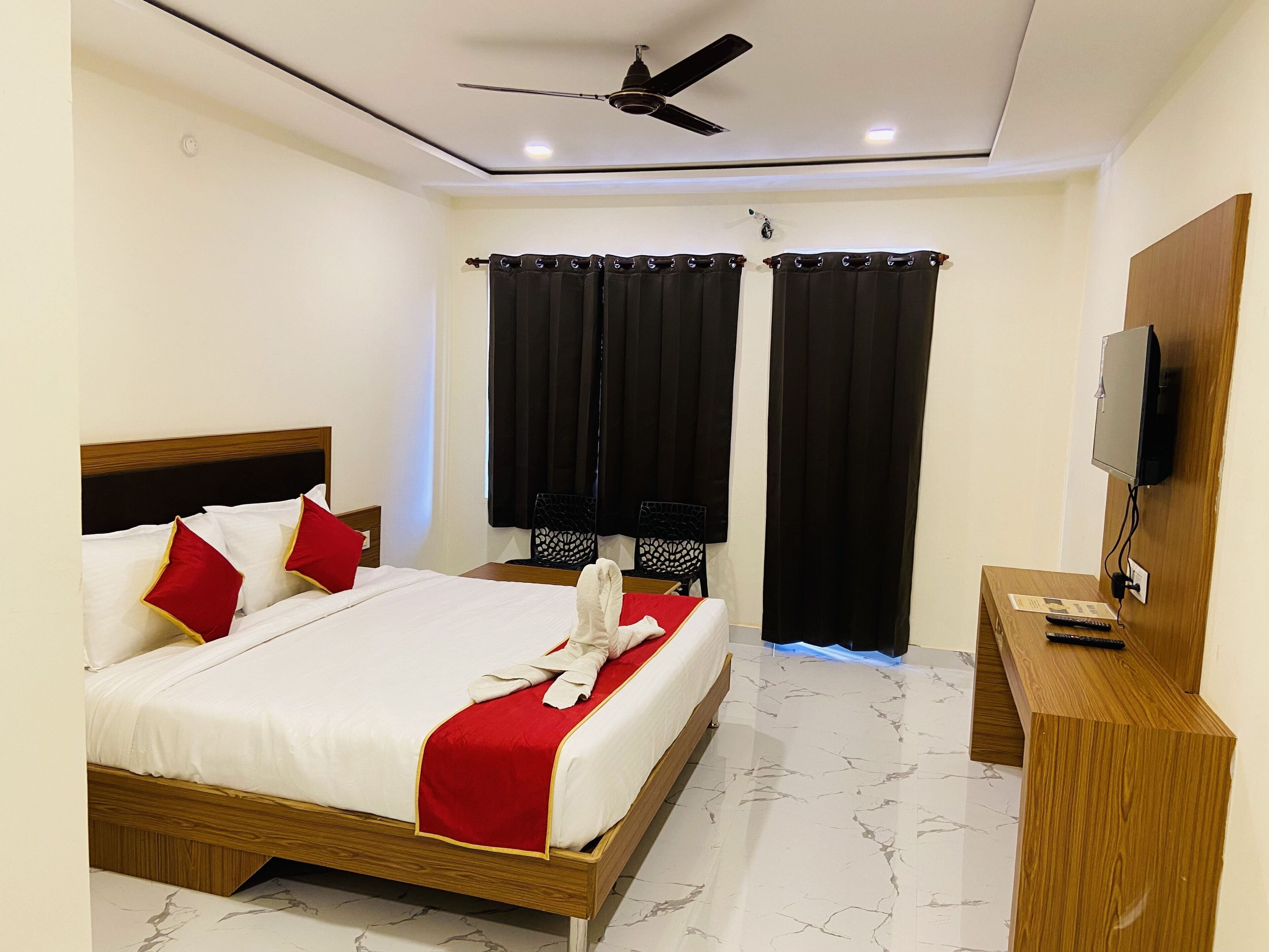 A hotel room with a bed, a ceiling fan, a TV, and a desk with a remote control.