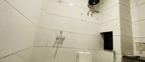 A bathroom with white marble tiles, a toilet, a shower, and a water heater.