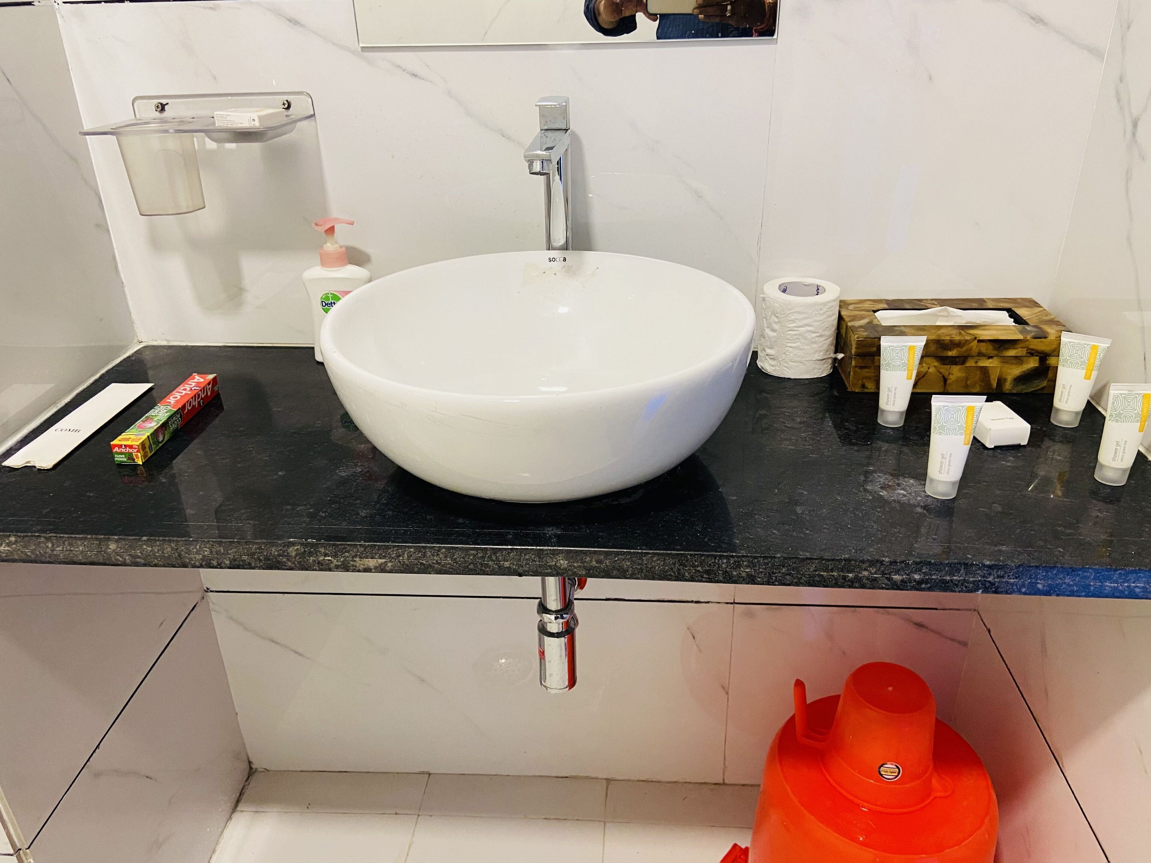 A bathroom with a white sink, a mirror, a towel dispenser, and toiletries on the countertop.