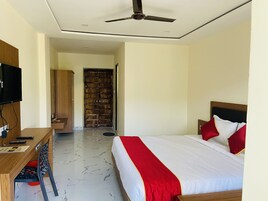 A hotel room with a bed, a desk with a TV, a wardrobe, and a door leading to another room.