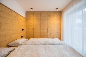 A bedroom with a wooden headboard, a bed with patterned bedding, and a window with sheer curtains.