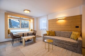 A modern living room with a wooden headboard, a sofa with cushions, a dining table with chairs, and a small round table.
