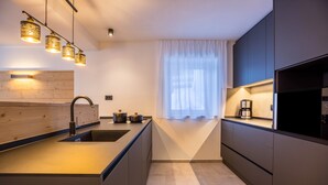 Una cocina moderna con una isla central, iluminación colgante y un ventanal con cortinas translúcidas.