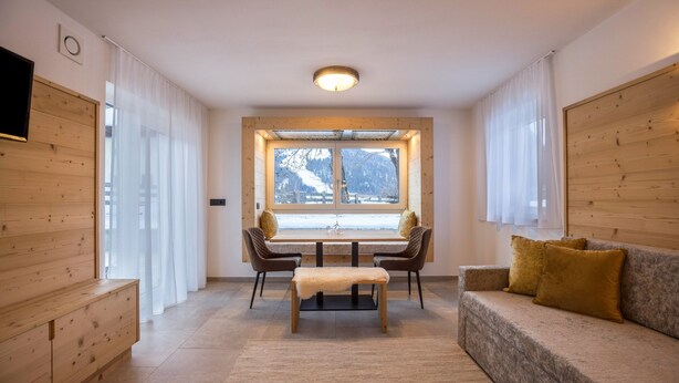 Un interior moderno con un banco de madera, un sofá con cojines, una mesa de comedor con sillas y un ventanal con vistas a las montañas.