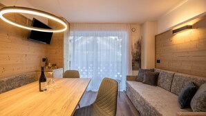 Een modern interieur met een houten eettafel, een bank, een aan de muur bevestigde televisie en een raam met dunne gordijnen.