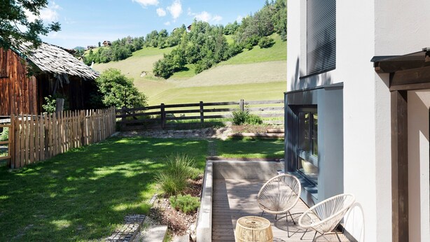 Een houten terras met rieten stoelen, een klein houten tafeltje en uitzicht op een heuvel.