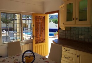 Une cuisine avec un coin repas, une vue sur la piscine et une porte donnant sur l’extérieur.