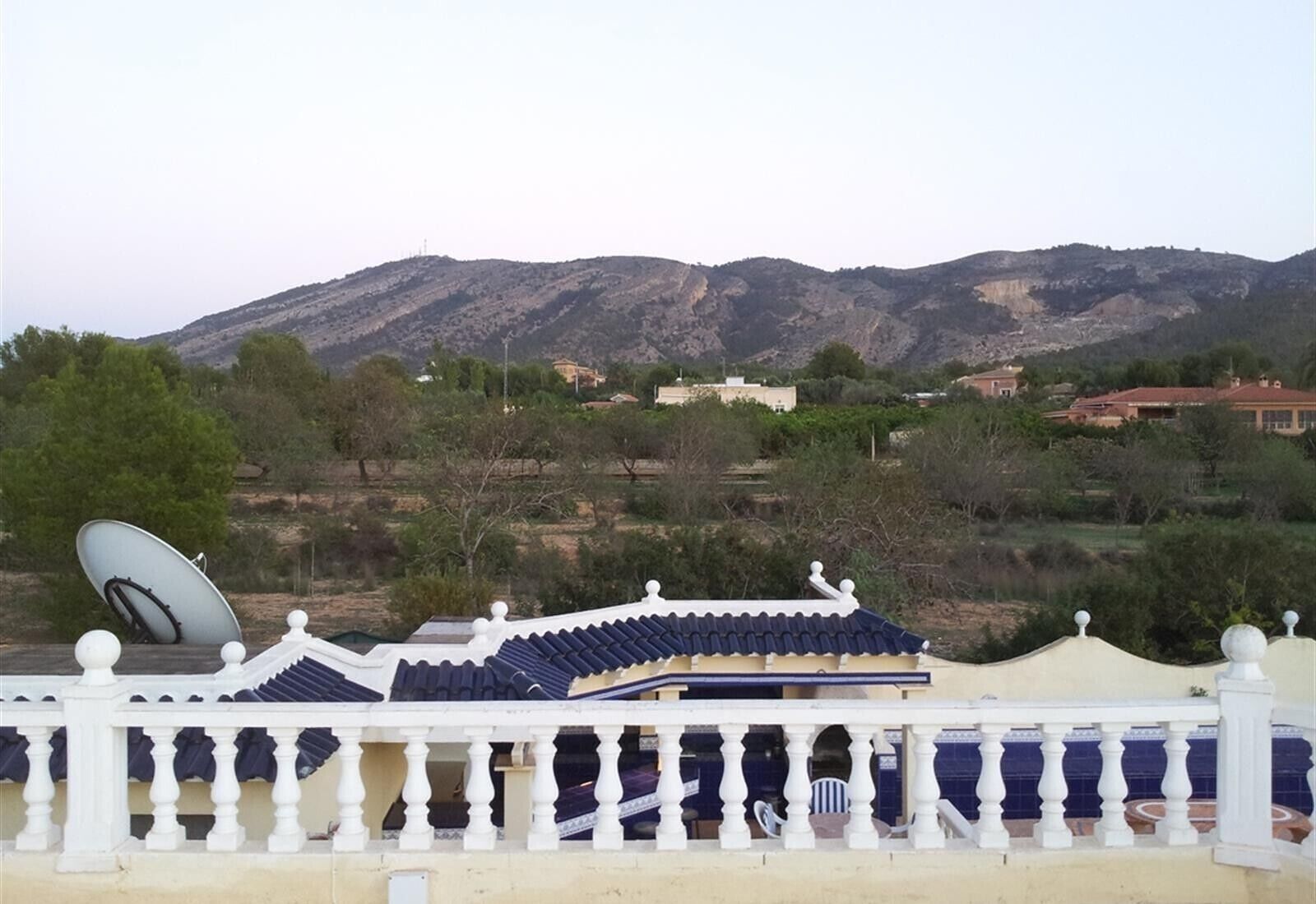 Un edificio con techo tradicional, una antena parabólica y vistas a montañas al fondo.