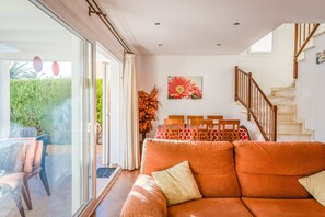 A living room with a sofa, a dining table with chairs, a staircase, and a large window.