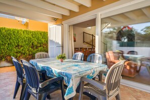 An outdoor patio with a table and chairs, a glass door leading to an interior space, and a green hedge.
