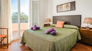 A hotel room with a bed, a nightstand, a lamp, a chair, and a sliding glass door leading to an outdoor area. - Villa "Lorena" with Pool, Garden & Wi-Fi (Ciutadella de Menorca)