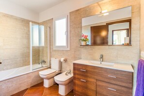 Un baño moderno con bañera, dos inodoros, un tocador con espejo y una ventana.