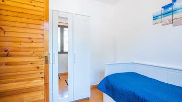 A bedroom with a wooden door, a white wardrobe, a bed with a blue cover, and a wall-mounted picture.