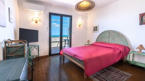 Un dormitorio con cama, una mesa, sillas, una lámpara y vista a la playa.