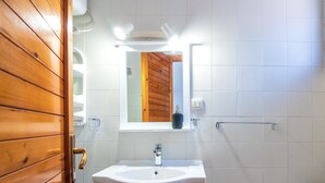 Un baño con puerta de madera, azulejos blancos, un lavabo blanco, un espejo y un perchero para toallas.