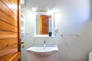 Ein Badezimmer mit Holztür, weißen Fliesen, einem weißen Waschbecken, einem Spiegel und einem Handtuchhalter.