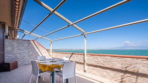 Un espacio comedor al aire libre techado con una mesa preparada para cuatro personas, con vista a un cuerpo de agua.