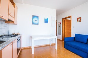 Eine Küche mit weißem Tisch und blauem Sofa, einem Herd und einer Holztür.