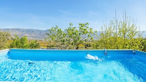 Une piscine d’eau cristalline, d’un bleu éclatant, avec en arrière-plan une vue sur des montagnes et des arbres.