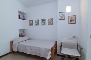 Une chambre à coucher avec un lit, une chaise, une étagère remplie de livres et des tableaux encadrés accrochés au mur.
