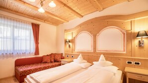 Una camera d'albergo con due letti, un divano, pannelli in legno e una finestra con tende.