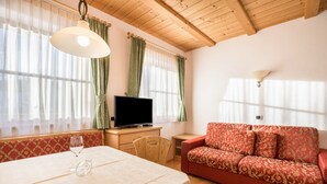 A room with a wooden ceiling, a television on a wooden table, a red patterned sofa, and a dining table with a glass. - Apartment 'Lisüra Boè' with Mountain View and Wi-Fi (Corvara)