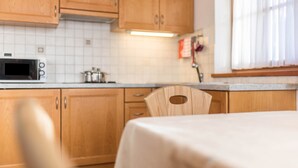 A kitchen with wooden cabinets, a microwave, and a table with a tablecloth. - Apartment 'Lisüra Boè' with Mountain View and Wi-Fi (Corvara)