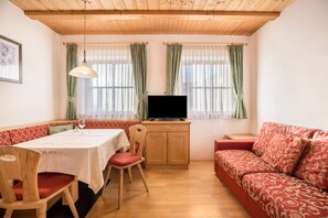 Ein gemütliches Zimmer mit Esstisch, Stühlen, einer Couch, einem Fernseher und einem Schrank.