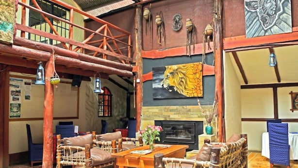 A rustic interior with a wooden staircase, a fireplace with a lion mural, and traditional woven furniture. - Kongoni Camp (Nanyuki)