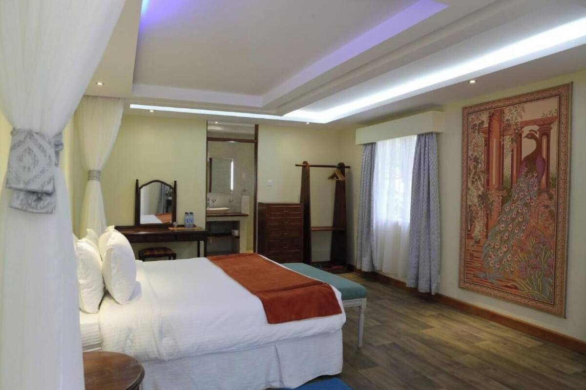 A hotel room with a bed, bedside table, mirror, wardrobe, and a large tapestry on the wall.