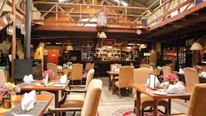 A restaurant with wooden beams, tables with floral centerpieces, and a bar area in the background. - Kongoni Camp (Nanyuki)