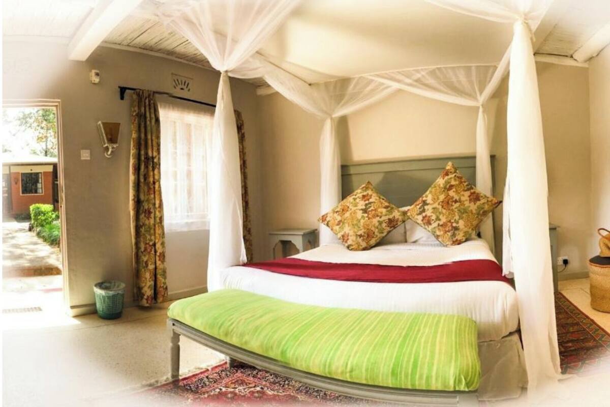 A bedroom with a four-poster bed, a green bench, and a red bedspread.