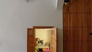 Habitació amb un armari de fusta, una taula petita amb llibres i joguines, i una estant amb diversos objectes.