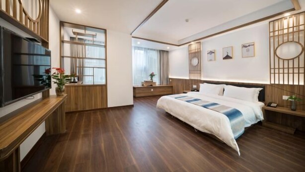 A modern hotel room with a large bed, wooden flooring, a TV, a desk, and a window with curtains. - Jiu Jian Tang Bo City Hotel (Ningde)