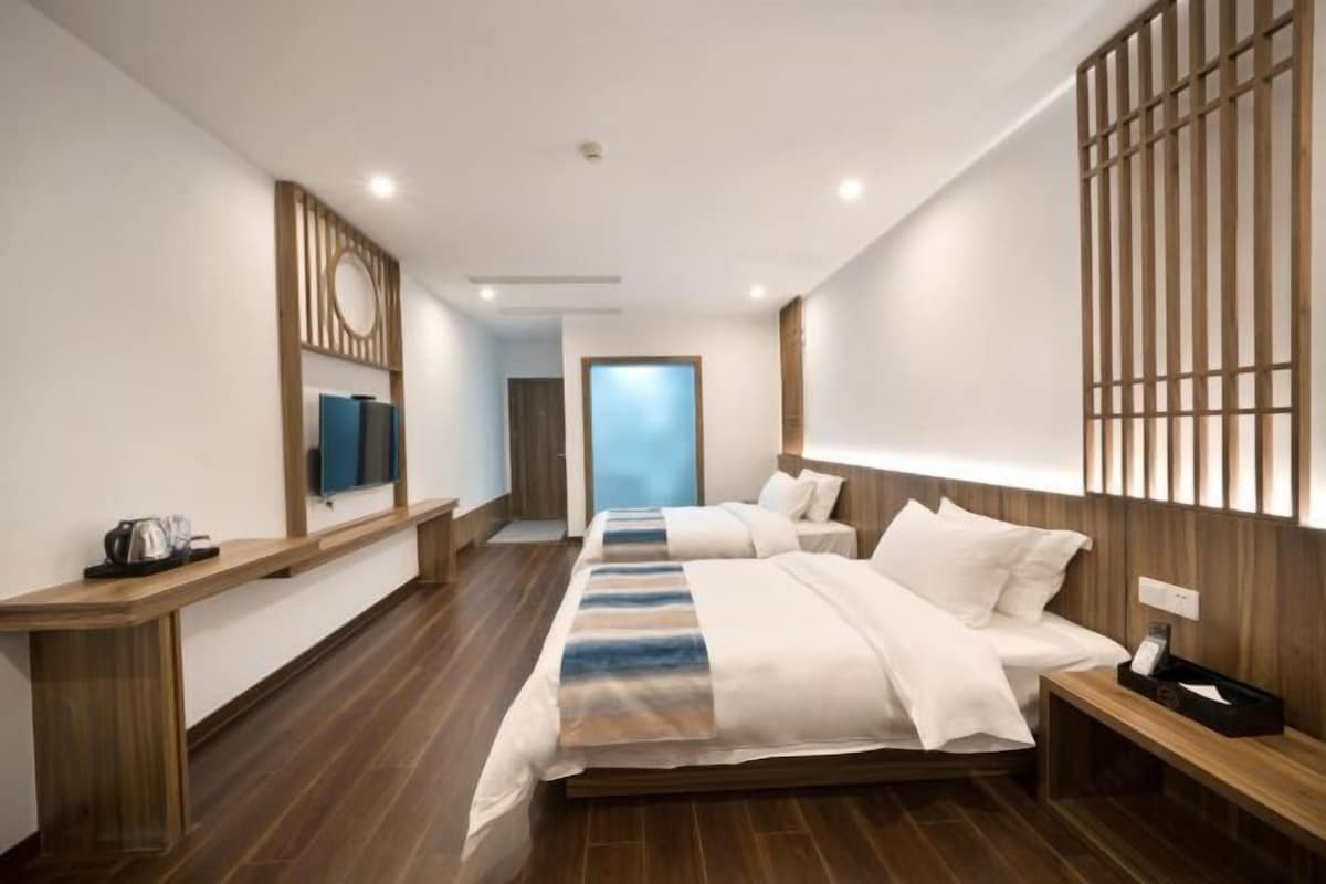 A modern hotel room with a large bed, a wooden bench, a TV, and a view of the outside.