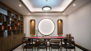 A dining area with a long table, six chairs, a central round mirror, and wooden shelving with red containers. - Jiu Jian Tang Bo City Hotel (Ningde)